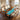 A custom epoxy resin burl cedar dining table featuring rich swirling grain and a translucent resin river, placed in a sunlit dining space with ocean views and elegant seating - BespokeTableCo