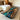 A live-edge golden camphor coffee table with a glossy resin top featuring turquoise, blue, and dark gray river-like patterns, placed in a bright living room next to a white sectional sofa, creating a warm and inviting atmosphere - BespokeTableCo