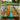 A handcrafted resin table with live-edge olive wood and vivid turquoise resin inlay, positioned in a contemporary dining room with light wood seating and a serene outdoor landscape visible in the background - BespokeTableCo