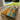 A large live-edge olive wood dining table with a bright turquoise resin river running through the center, surrounded by light wood dining chairs in a bright dining room with an outdoor pool and lawn visible through the windows - BespokeTableCo