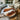 Custom epoxy resin walnut coffee table featuring a round wooden top with white resin finish, placed in a sunlit contemporary kitchen space with wicker seating and warm home decor - BespokeTableCo